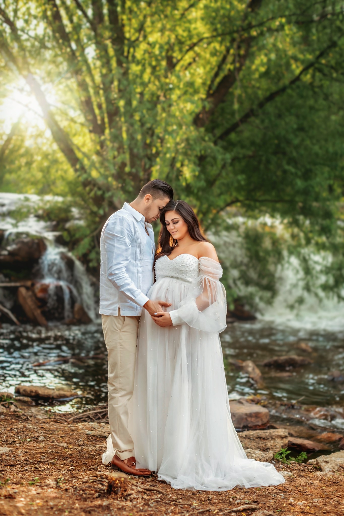 Couple posing together awaiting their sweet newborn baby in front of the waterfall.