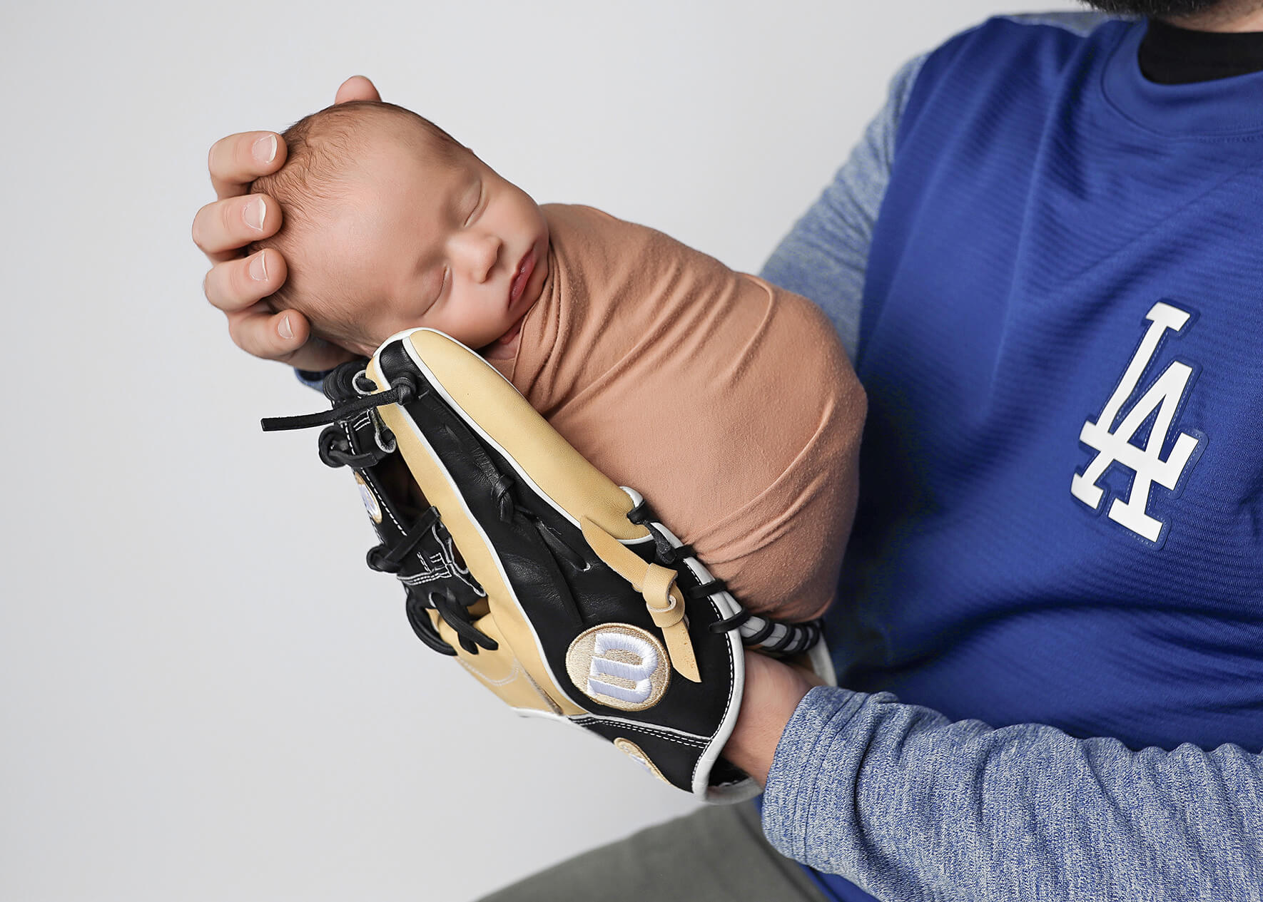 Sleeping newborn posing in dad's baseball glove sporting their favorite team, the LA Dodgers.