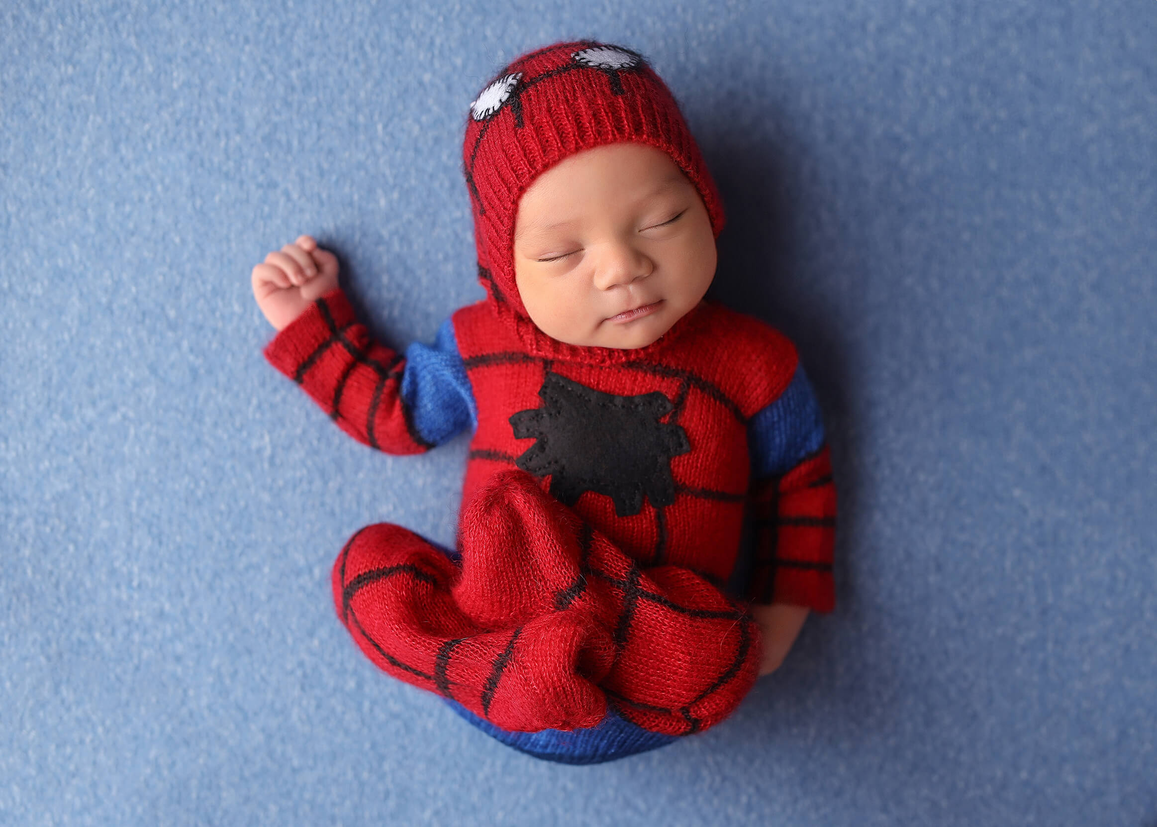 Newborn baby wearing a spiderman onesy posing on blue beanbag blanket after bundling their maternity and newborn sessions.