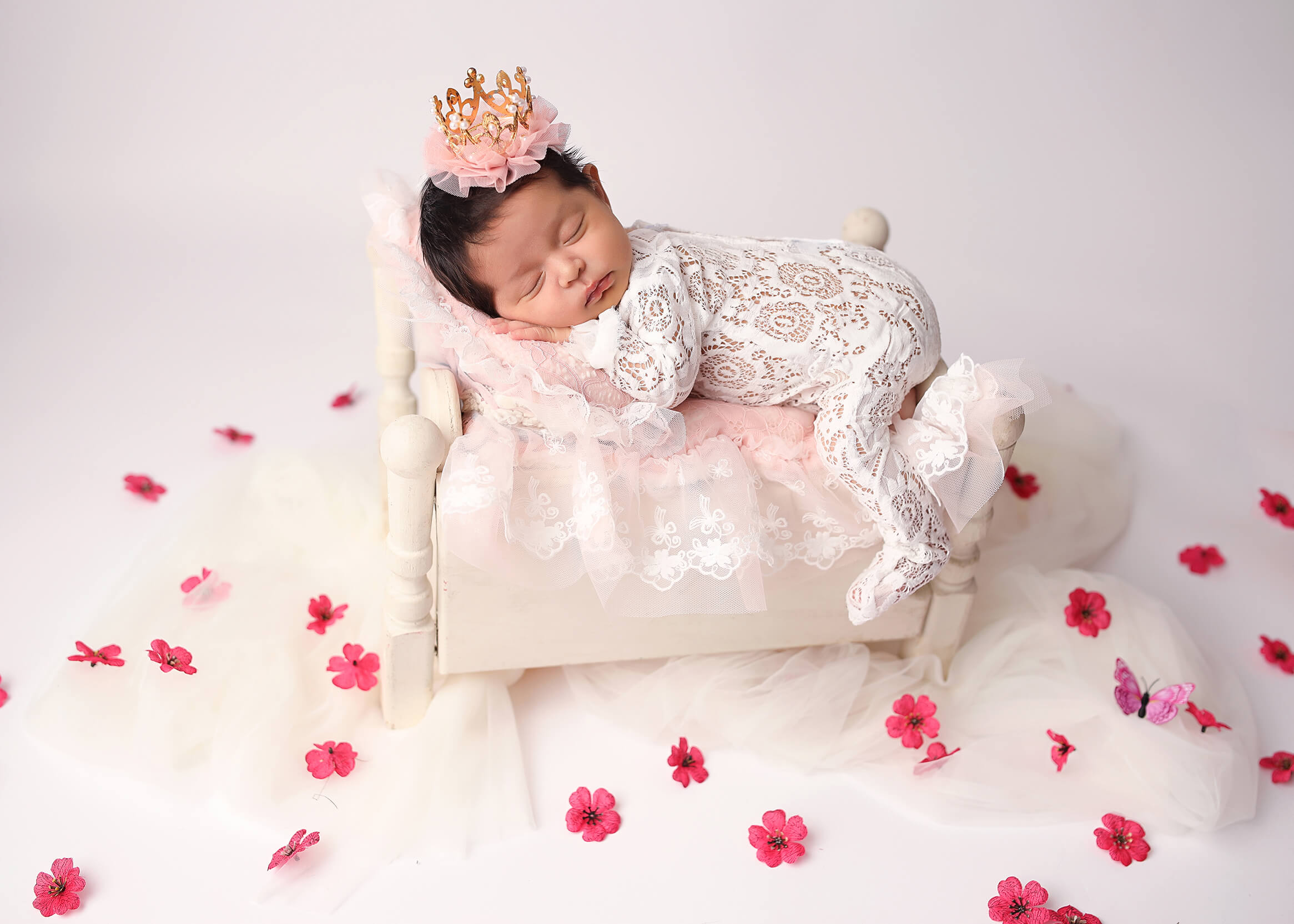 Gorgeous newborn posing in beautiful white lace laying on vintage white bed.