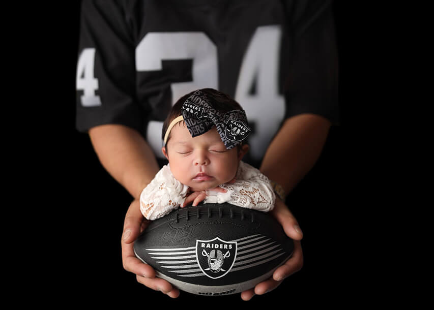 Adorable baby in Dad's arms wearing his Las Vegas Raiders gear at his Denver newborn photography session.