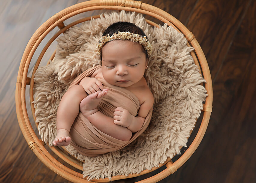 Beautiful sleeping newborn baby wrapped in a tan wrap on a wicker vintage chair at her denver newborn photography session.