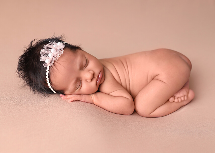 Newborn baby sleeping on a light pink beanbag blanket posing at her denver newborn photography session.