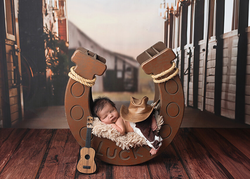 Cowboy themed newborn shot with babe sleeping on wooden horsehoe prop at his newborn photos denver photography session.