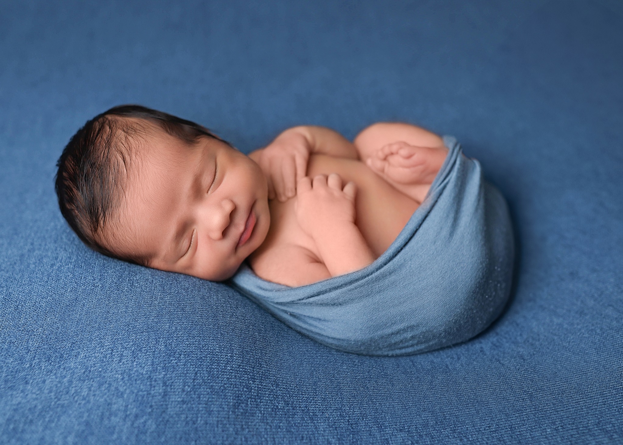 Cute newborn posing wrapped up on gorgeous blue beanbag blanket