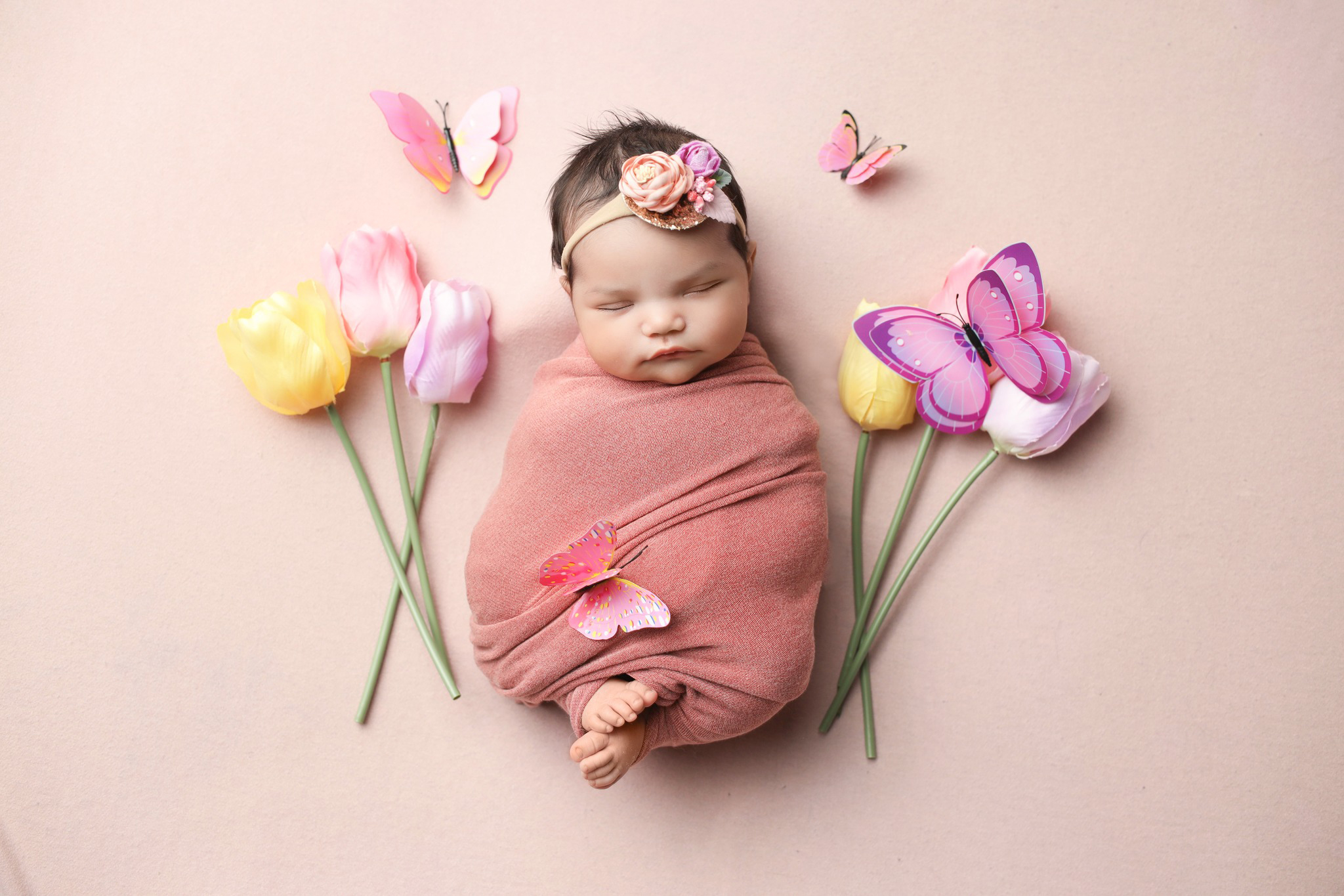 Newborn baby posing in blush pink wrap surrounded by tulips right after her Boulder pediatricians appointment.