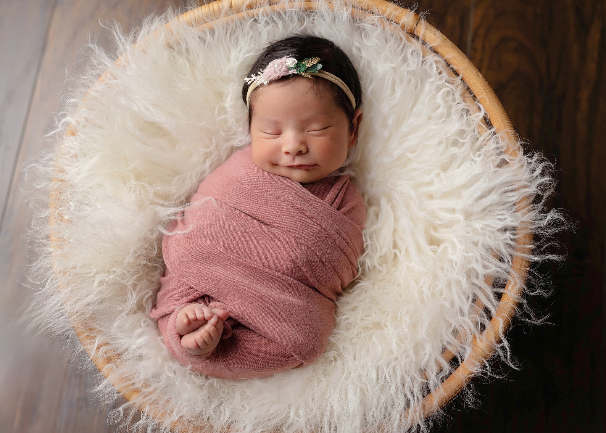 Newborn baby sleeping in blush wrap in round wicker bed, right after her Broomfield pediatricians appointment.